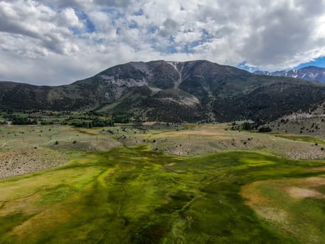 Aerial view of green land and small curve river with mountain in the background in Aspen Springs, Mono County California, USA