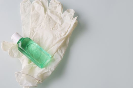 Top view of sanitizing gel for medical purpose and rubber gloves on a grey background. Space for text