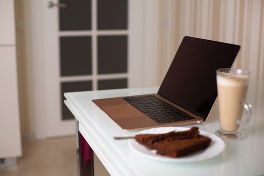 Rose gold laptop with a glass of coffee and homemade chocolate cake on the table. Study at home concept