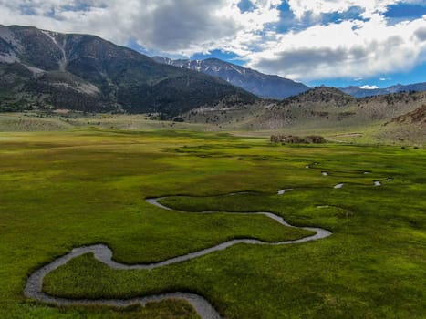 Aerial view of green land and small curve river with mountain in the background in Aspen Springs, Mono County California, USA