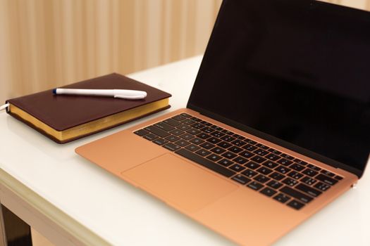 Comfortable workplace at home. Laptop with diary and pen on a white table