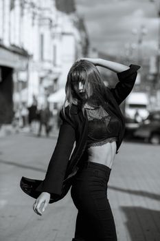 Street portrait of attractive woman with long hair wears lingerie and jacket posing at the street in Kyiv. Monochrome color