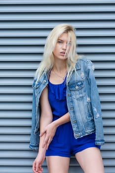 Street photosession of glamor blonde woman wears casual apparel posing near the metal shutters