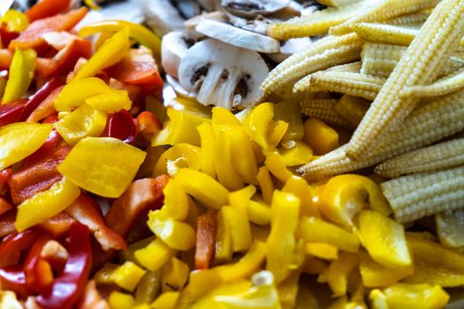 Mix of multicolored vegetables with mushrooms, baby corn, yellow chilli peppers and more cur for a vegetarian dish. Shows preparation of a dish at home with some fresh healthy ingridients