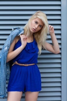 Street photosession of fashionable blonde woman wears casual apparel posing near the metal shutters