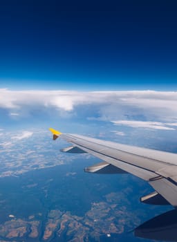 View of the wing of an airplane flying above the clouds at high altitude under a blue sky from the passenger window. In flight over Europe. View of jet airplane wing flying in blue sky over clouds.