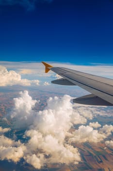 View of the wing of an airplane flying above the clouds at high altitude under a blue sky from the passenger window. In flight over Europe. View of jet airplane wing flying in blue sky over clouds.