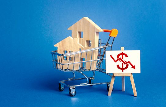 Wooden houses in a shopping cart and an easel with a red dollar arrow down chart. Fall of real estate market. Cheap rent. Reduced demand, recession. Low sales. Value cost decrease. Bad attractiveness.