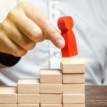 A man puts a red human figure on top of the stairs. Career growth, improvement of skills. Promotion at work of employees to leading post. The concept of success. Training. Education, business