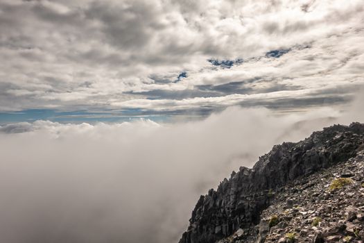 Haleakala Volcano, Maui, Hawaii, USA. - January 13, 2020: Crater filled by huge white-gray cloud. Black rocks of edge. Under cloudscape with blue patches.