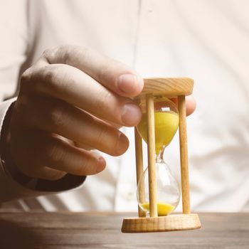 The person holds an hourglass in his hands. Business management. Logistics, process efficiency, savings. Time management. Awareness of time constraints. Pension, countdown, deadline. Self discipline