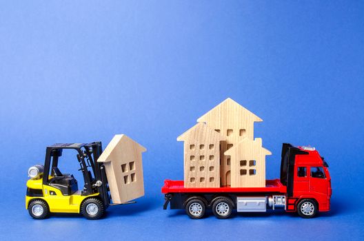 A yellow forklift loads a house figures on a red truck. Concept of transportation and cargo shipping, moving company. Construction of new houses and objects. Industry. Move entire buildings.