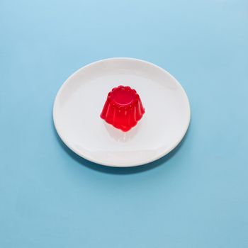 Close-up of a strawberry jelly dessert on a white plate with a light blue background