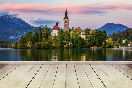 Empty wooden table in front of abstract blurred background in nature, can be used for display or montage your products. Mock up for display of product. Bled island in the background from Slovenia.