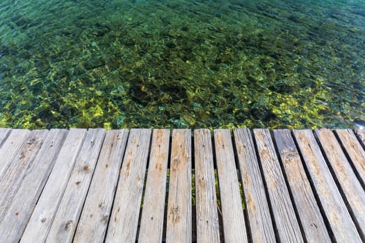 Wooden board empty over sea, can be used for display or present a product. Summer season. Empty perspective wooden planks over the reflection of green water, product display template.