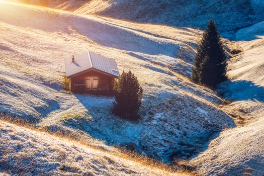 Small wooden farm house, cottage or log cabins on meadow on Alpe di Siusi, Seiser Alm. Alpe di Siusi or Seiser Alm with Sassolungo, Langkofel mountain group, Dolomite Alps, South Tyrol, Italy.