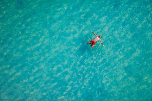 Drone view of a man floating in tropical sea water. Aerial view of young man floating on sea water enjoying sunbathing and vacations in tropical destination. People travel tourism holidays concept. 