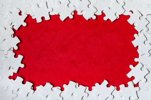 Framing in the form of a rectangle, made of a white jigsaw puzzle. Frame text and jigsaw puzzles. Frame made of jigsaw puzzle pieces on red background.