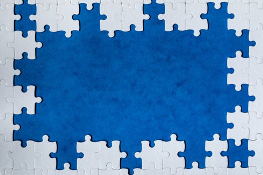 Framing in the form of a rectangle, made of a white jigsaw puzzle. Frame text and jigsaw puzzles. Frame made of jigsaw puzzle pieces on blue background.