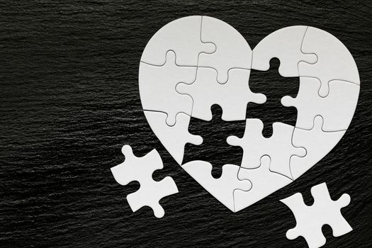 Heart-shaped jigsaw puzzle on color background. Puzzle heart on wooden background. A missing piece of the heart puzzle. Heart shape jigsaw puzzle. Puzzles in the shape of a heart. 