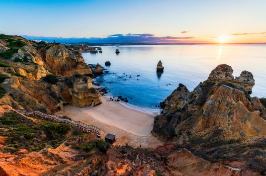 Sunrise at Camilo beach in Lagos, Algarve, Portugal. Wooden footbridge to the beach Praia do Camilo, Portugal. Picturesque view of Praia do Camilo beach in Lagos, Algarve region, Portugal.