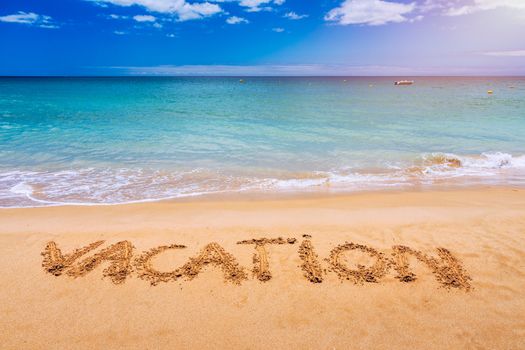 Vacation text on a beach. Vacation written in a sandy tropical beach. "Vacation" written in the sand on the beach blue waves in the background. Vacation on the sand beach concept.