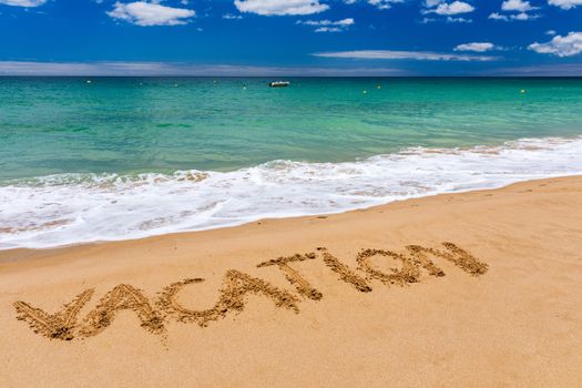 Vacation text on a beach. Vacation written in a sandy tropical beach. "Vacation" written in the sand on the beach blue waves in the background. Vacation on the sand beach concept.