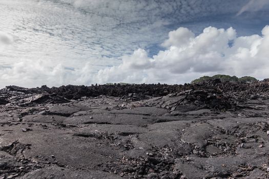 Leilani Estate, Hawaii, USA. - January 14, 2020: Large 2018 Kilauea volcano eruption hardened black lava field under white cloudscape and some green trees on horizon peeping above.