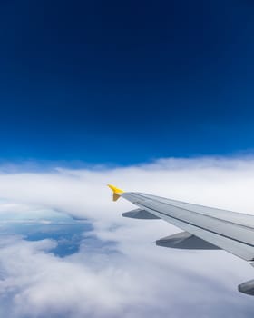 View of the wing of an airplane flying above the clouds at high altitude under a blue sky from the passenger window. In flight over Europe. View of jet airplane wing flying in blue sky over clouds.