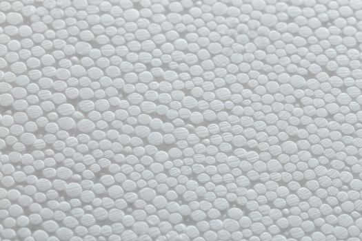 Simple close-up flat but bumpy background of white polystyrene foam or styrofoam, white on white backdrop with selective focus.