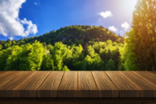 Empty wooden table for product placement or montage with focus to table top in the foreground. Mock up for display of product. Beautiful background with forest, waterfall, incredible landscape.