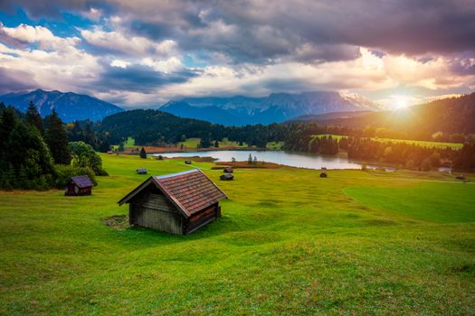 Panoramic morning scene of Wagenbruchsee (Geroldsee) lake with Zugspitze mountain range on background. Amazing autumn view of Bavarian Alps, Germany, Europe. Wooden hut on meadow by Geroldsee lake. 