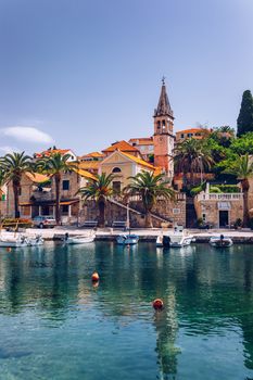 Church building and palm tree against sunny blue sky in Splitska village on Brac island, Croatia. 