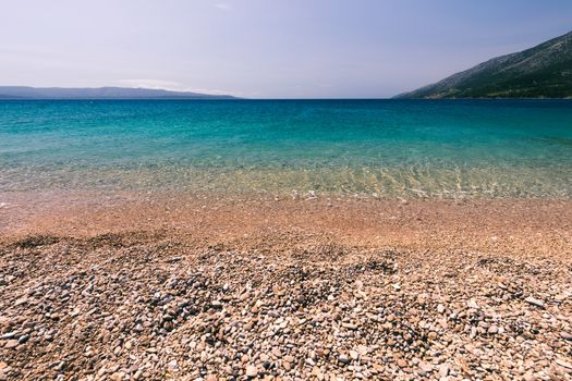 Stones under water. Sea pebbles on the beach. Sea pebbles on the beach sand with transparent water. Natural sea stones closeup. Beach smooth pebbles. Tourism and travel themed. Vacation background. 