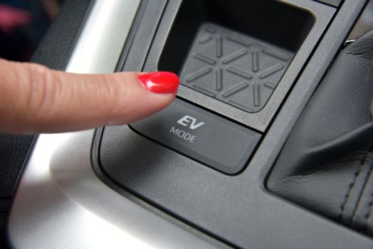 the finger of a woman on the switch for the ev mode of a hybrid car
