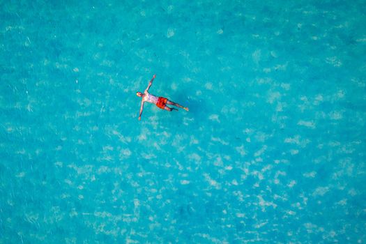 Drone view of a man floating in tropical sea water. Aerial view of young man floating on sea water enjoying sunbathing and vacations in tropical destination. People travel tourism holidays concept. 