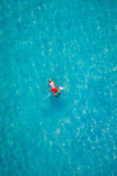 Drone view of a man floating in tropical sea water. Aerial view of young man floating on sea water enjoying sunbathing and vacations in tropical destination. People travel tourism holidays concept. 