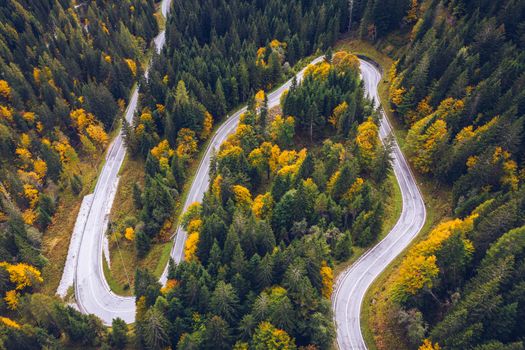 Curved bending road in the forest. Aerial image of a road. Forrest pattern. Scenic curvy road seen from a drone in autumn. Aerial top down view of zig zag winding mountain road, drone shot.
