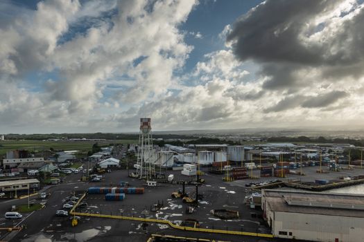 Hilo, Hawaii, USA. - January 14, 2020: Long evening shot over most of local port with tanks, stacked shipping containers, quays, warehouse, trucks, cars and more. All under brown cloudscape.