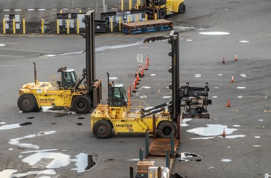 Hilo, Hawaii, USA. - January 14, 2020: Ocean port. closeup of 2 yellow-black Hyster shipping container lift trucks parked on gray tarmac with water pools.