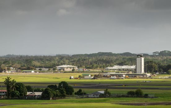 Hilo, Hawaii, USA. - January 14, 2020: Green airport with white control tower and buildings under dark rainty sky. Forest on horizon. Farm up front.