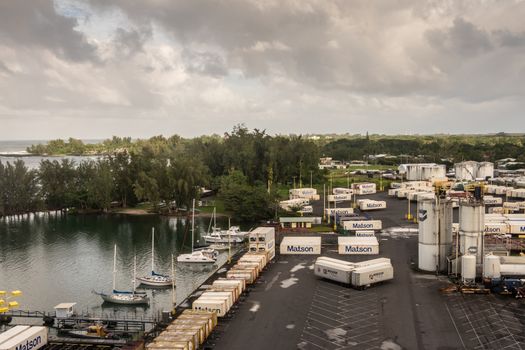 Hilo, Hawaii, USA. - January 14, 2020: Ocean port. Quay with White fuel tanks surrounded by Matson shipping containers placed on trailers. Green tree on horizon under cloudscape.