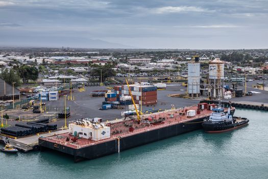 Kahului, Maui,, Hawaii, USA. - January 13, 2020: Nale double hull liquid tank barge docked at container quay in azure water port under light blue cloudscape. Buildings of town in back.