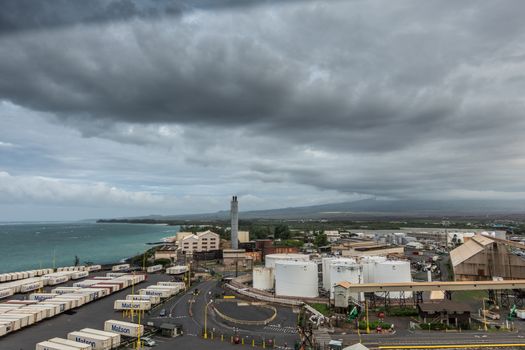 Kahului, Maui,, Hawaii, USA. - January 13, 2020: Huge dark cloud in full gray cloudscape hangs over the port area with its fuel tanks and shipping containers. Azure ocean and green zone in back.