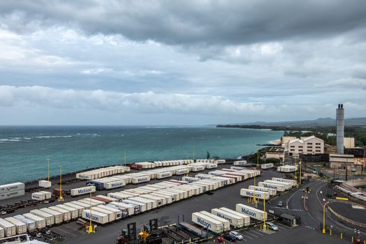 Kahului, Maui,, Hawaii, USA. - January 13, 2020: Matson shipping container yard full of white boxes on quay bordering azure ocean under gray rainy cloudscape. Old sugarcane processing plant.