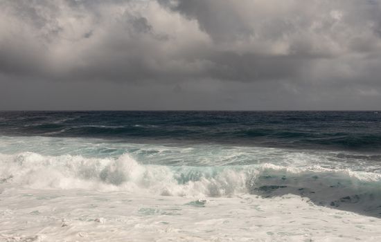 Kaimu Beach, Hawaii, USA. - January 14, 2020: Dark ocean under heavy gray rain cloudscape produces white surf when azure wave turns and crashes.