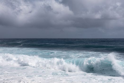 Kaimu Beach, Hawaii, USA. - January 14, 2020: Dark ocean under heavy gray rain cloudscape produces white surf when azure wave turns and crashes.