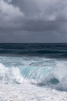 Kaimu Beach, Hawaii, USA. - January 14, 2020: Portrait of Dark ocean under heavy gray rain cloudscape produces white surf when azure wave turns and crashes.