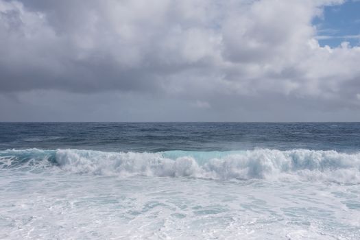 Kaimu Beach, Hawaii, USA. - January 14, 2020: Portrait of gray ocean under white cloudscape with blue patch produces white surf when azure wave turns and crashes.