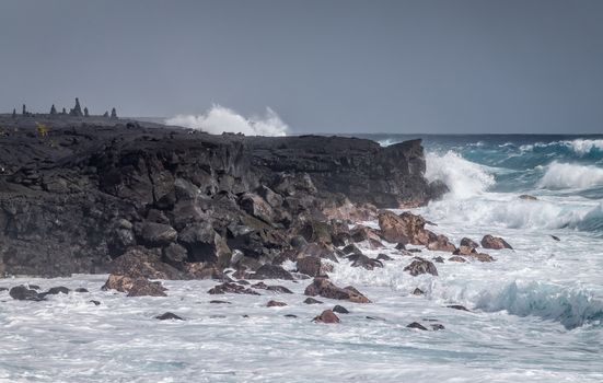 Kaimu Beach, Hawaii, USA. - January 14, 2020: Azure waves crash with white surf on black lava coastline under heavy rain gray cloudscape. 